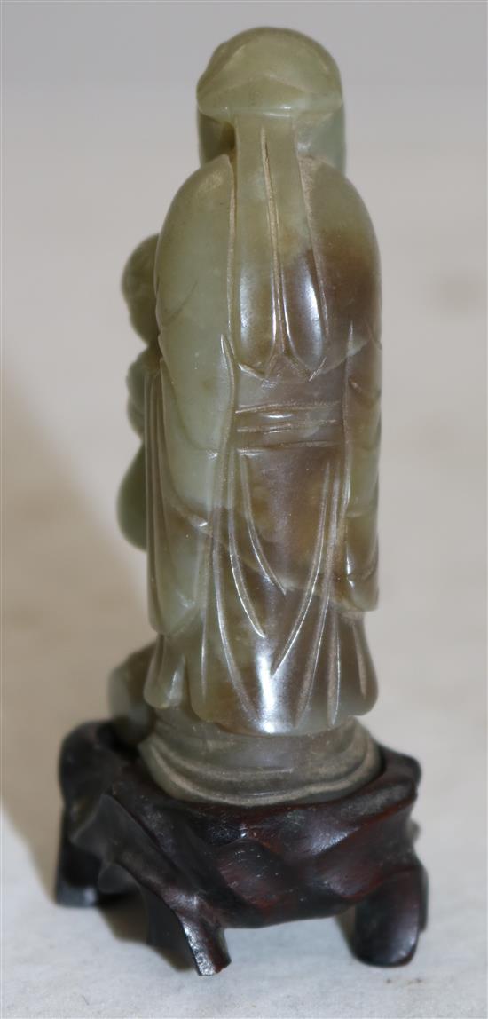 A Chinese celadon and brown jade group of Shou Lao and a boy standing upon a barrel, 18th/19th century, 7.3cm, ebonised wood stand